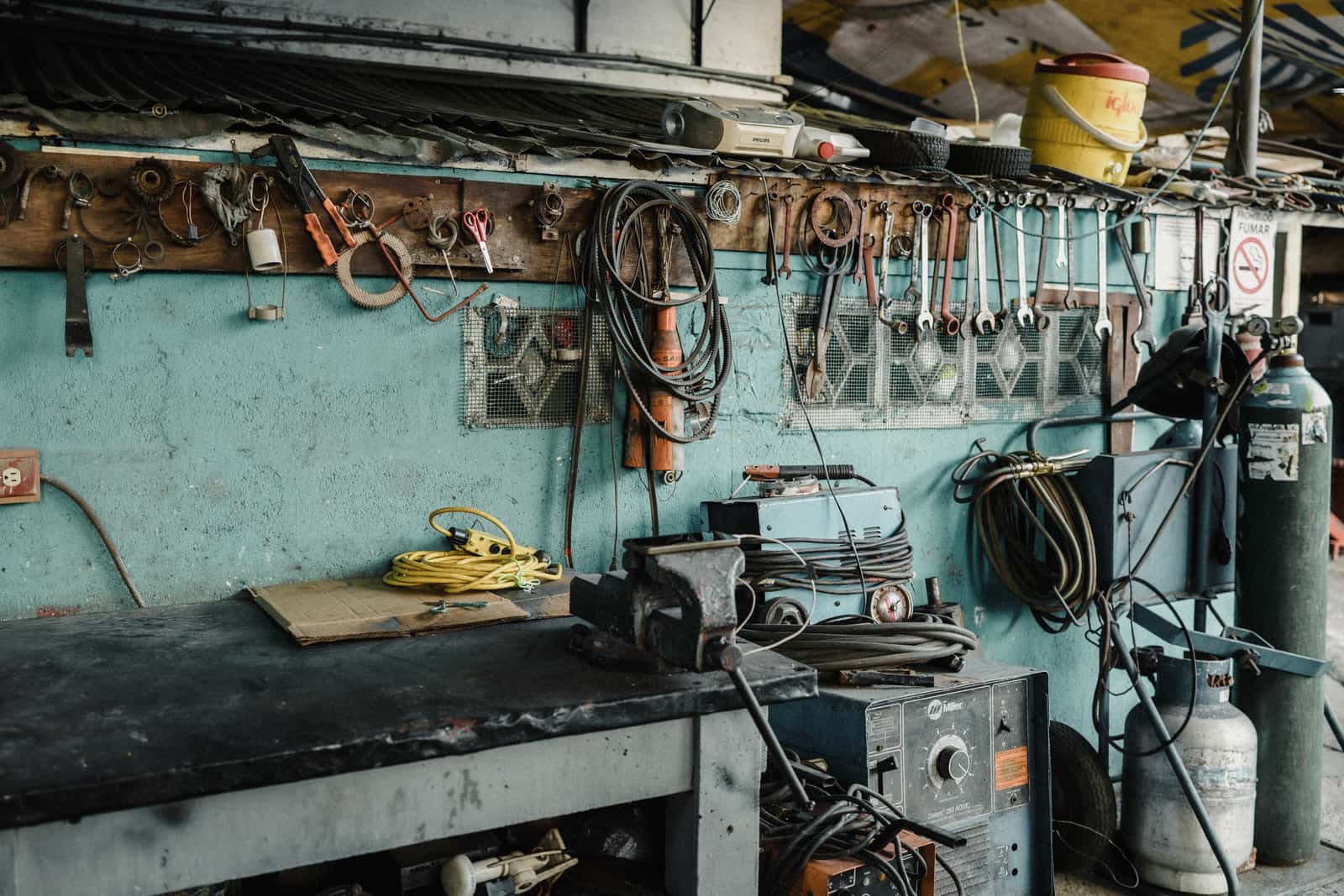 A busy workshop bench with a vise, tools and machinery around it