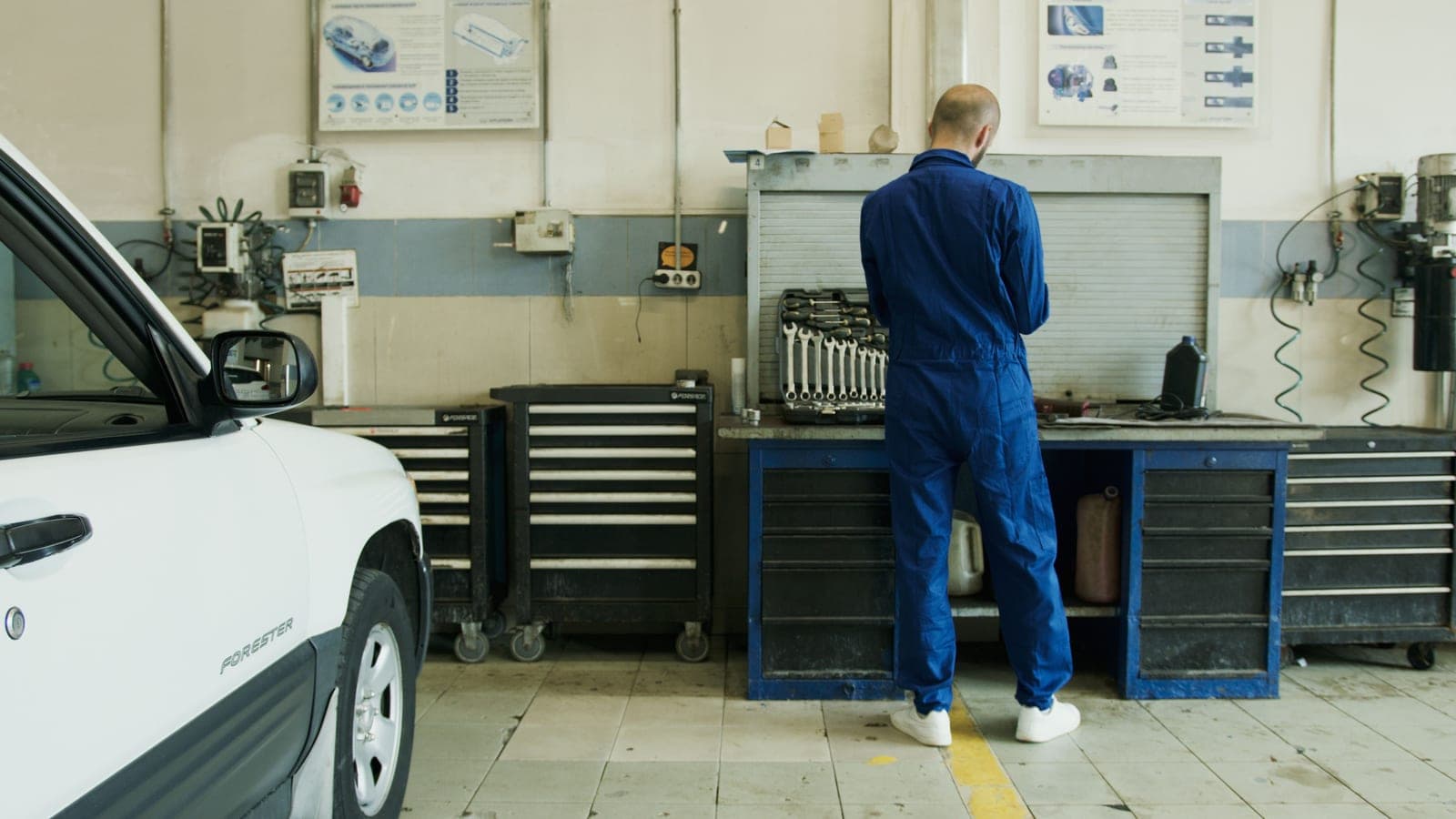 A mechanic in overalls working beside a car in a well-equipped garage