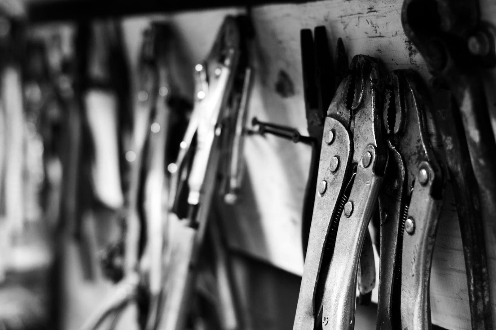 Locking pliers and hand tools hanging on a workshop rack, in black and white