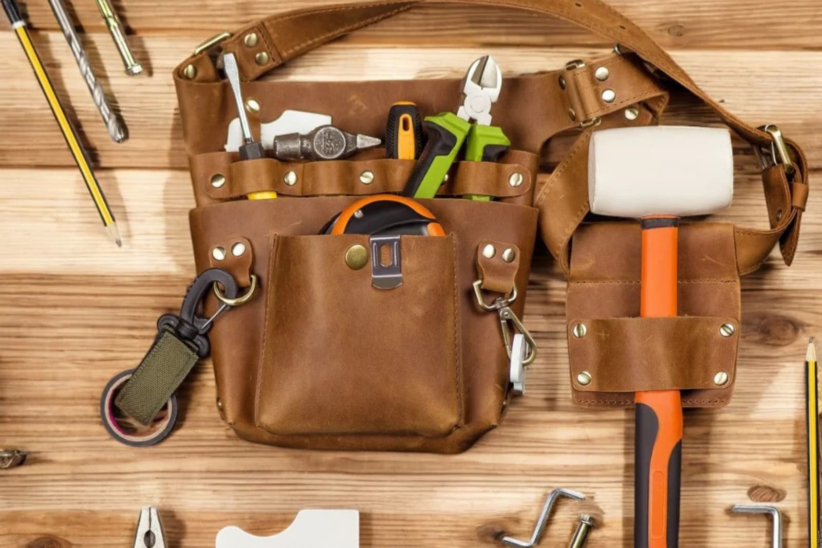 A leather tool belt loaded with carpenter hand tools on a wooden table