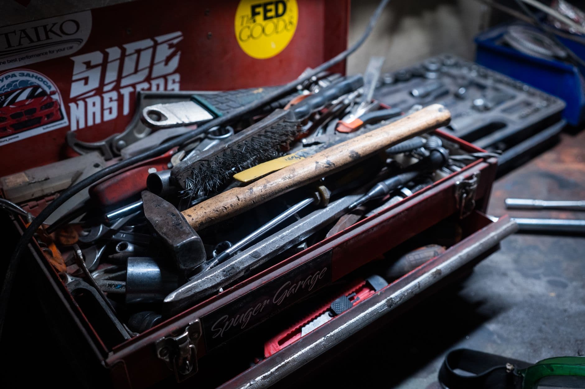 An overloaded red metal tool box in a garage, packed with a hammer, wrenches and a wire brush