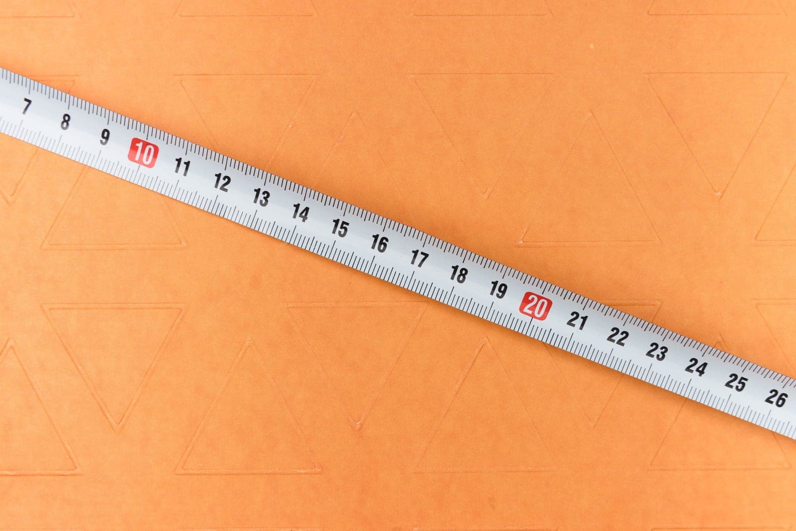 A metal measuring tape extended diagonally across an orange surface