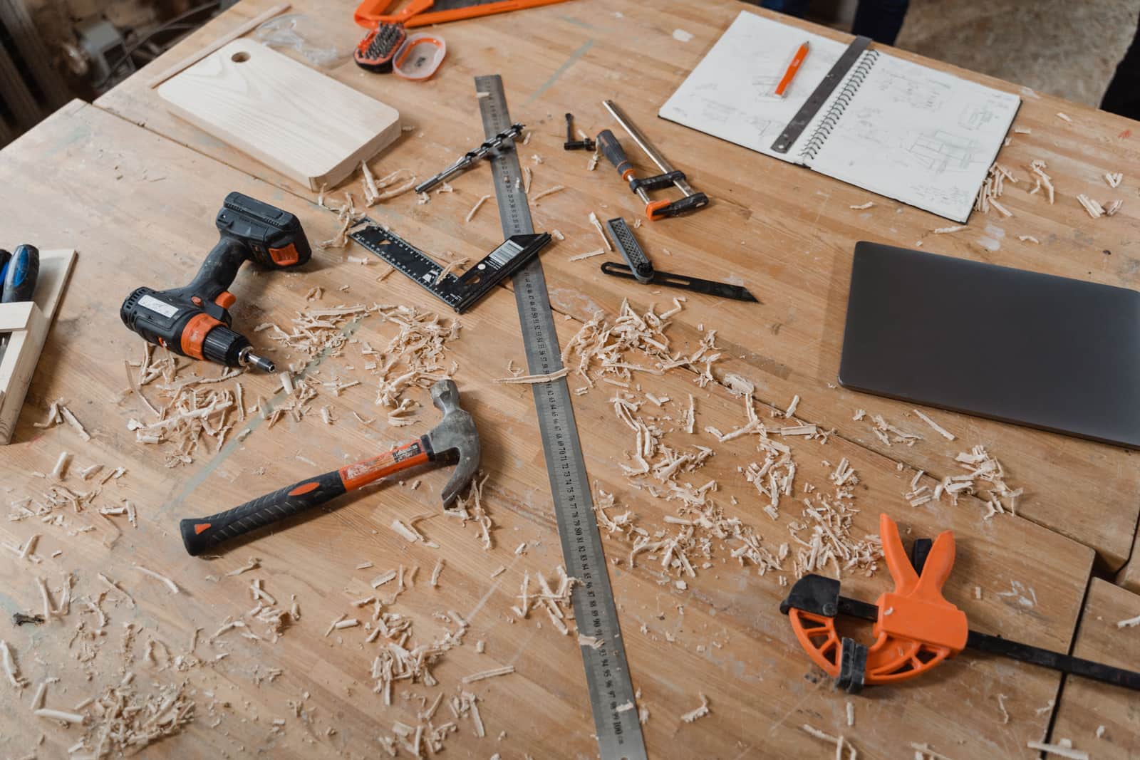 A workbench with woodworking tools, sketches and shavings across it