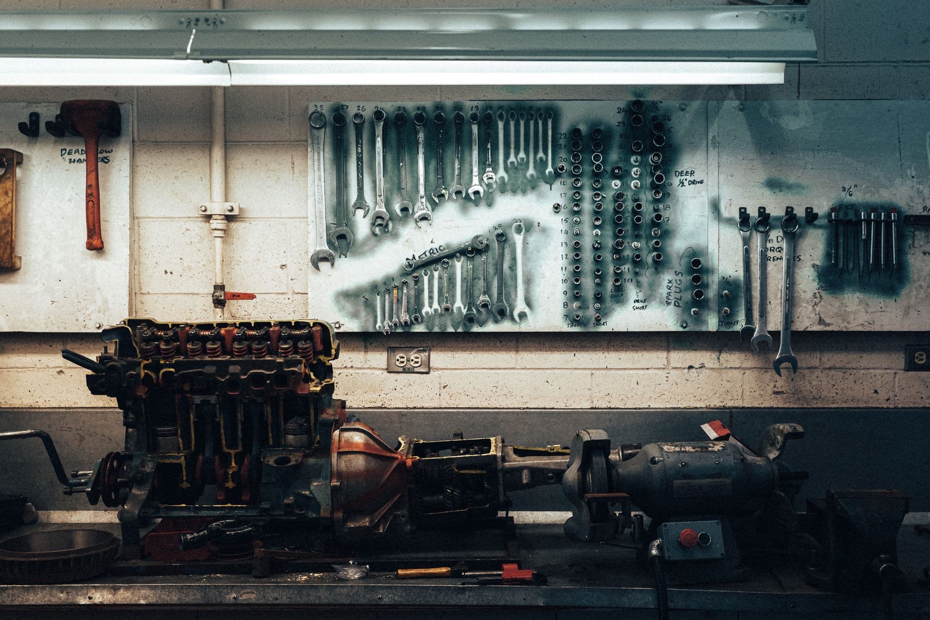 A mechanics workbench holding an engine and gearbox below a wall board of wrenches and sockets