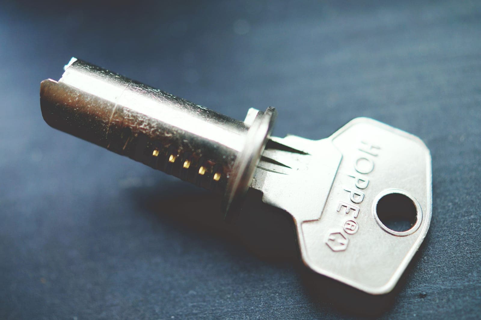 A tubular key beside its lock cylinder on a dark surface