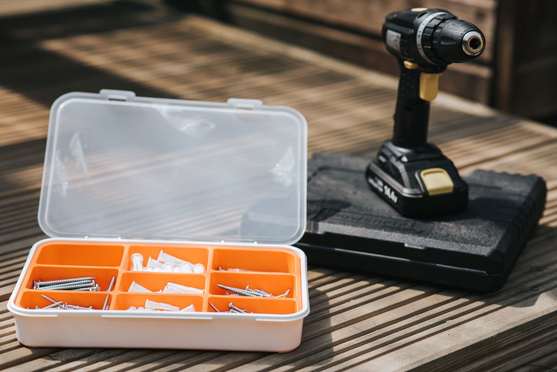 A cordless screwdriver resting on a tool case beside screws and bolts