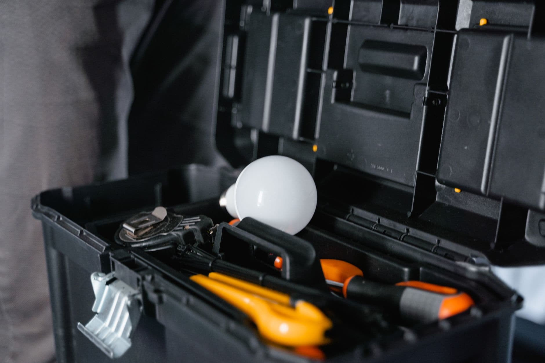 An open toolbox holding assorted hand tools and a light bulb