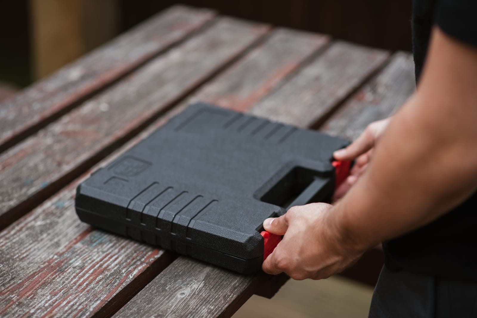 A craftsman packing a black tool box on a wooden table in daylight