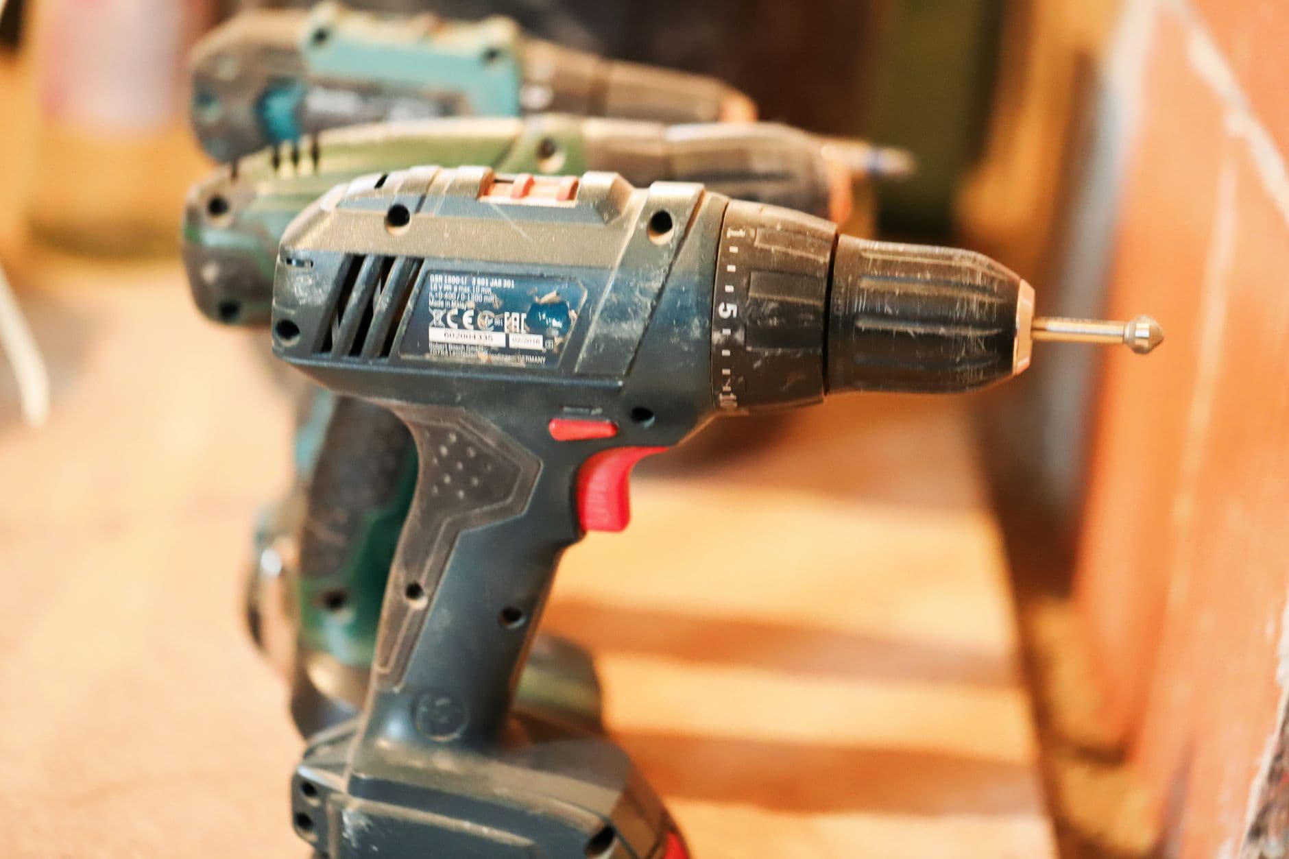 A row of well-used cordless drills standing on a wooden workbench