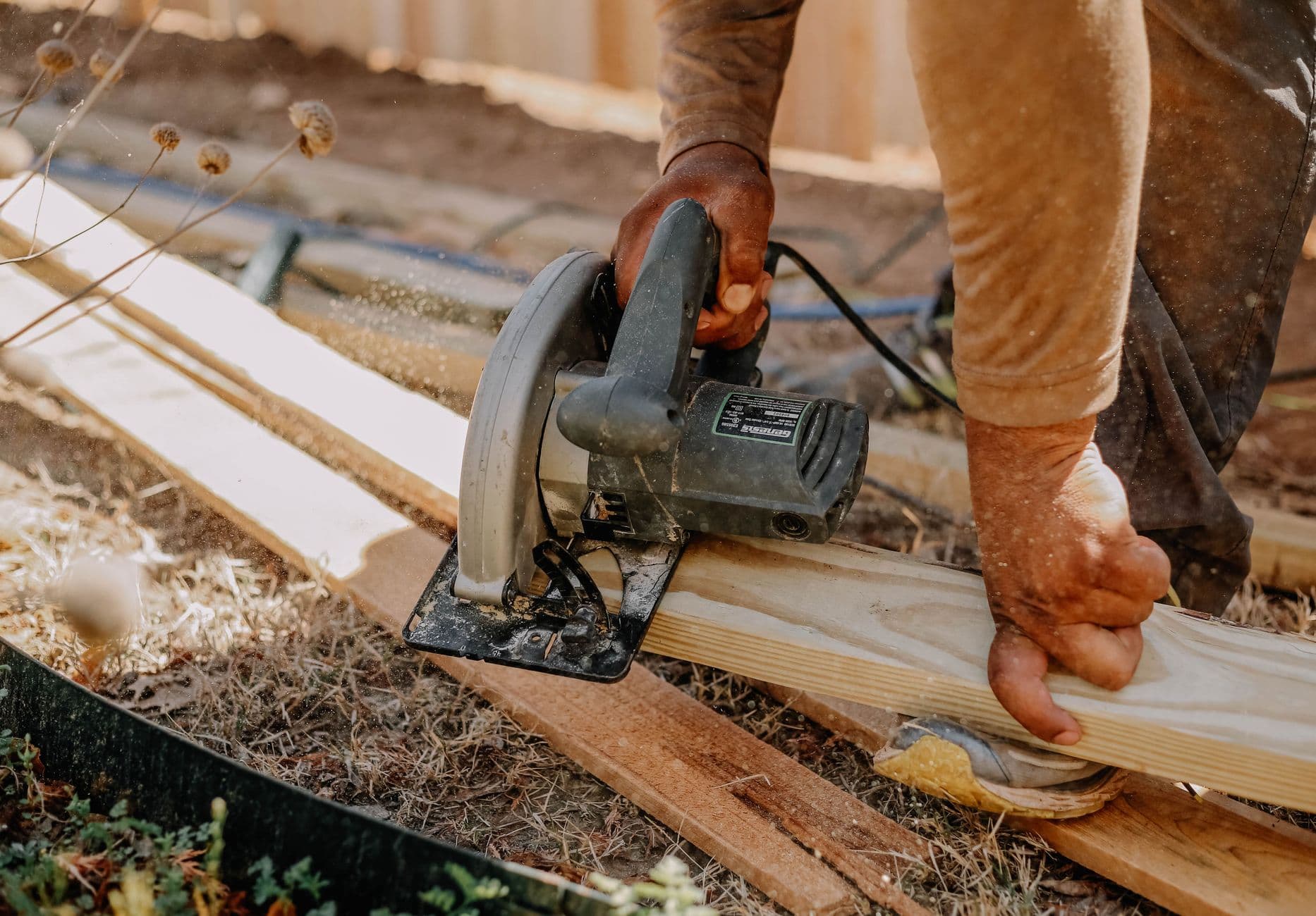 A carpenter cutting wooden planks with a circular saw outdoors