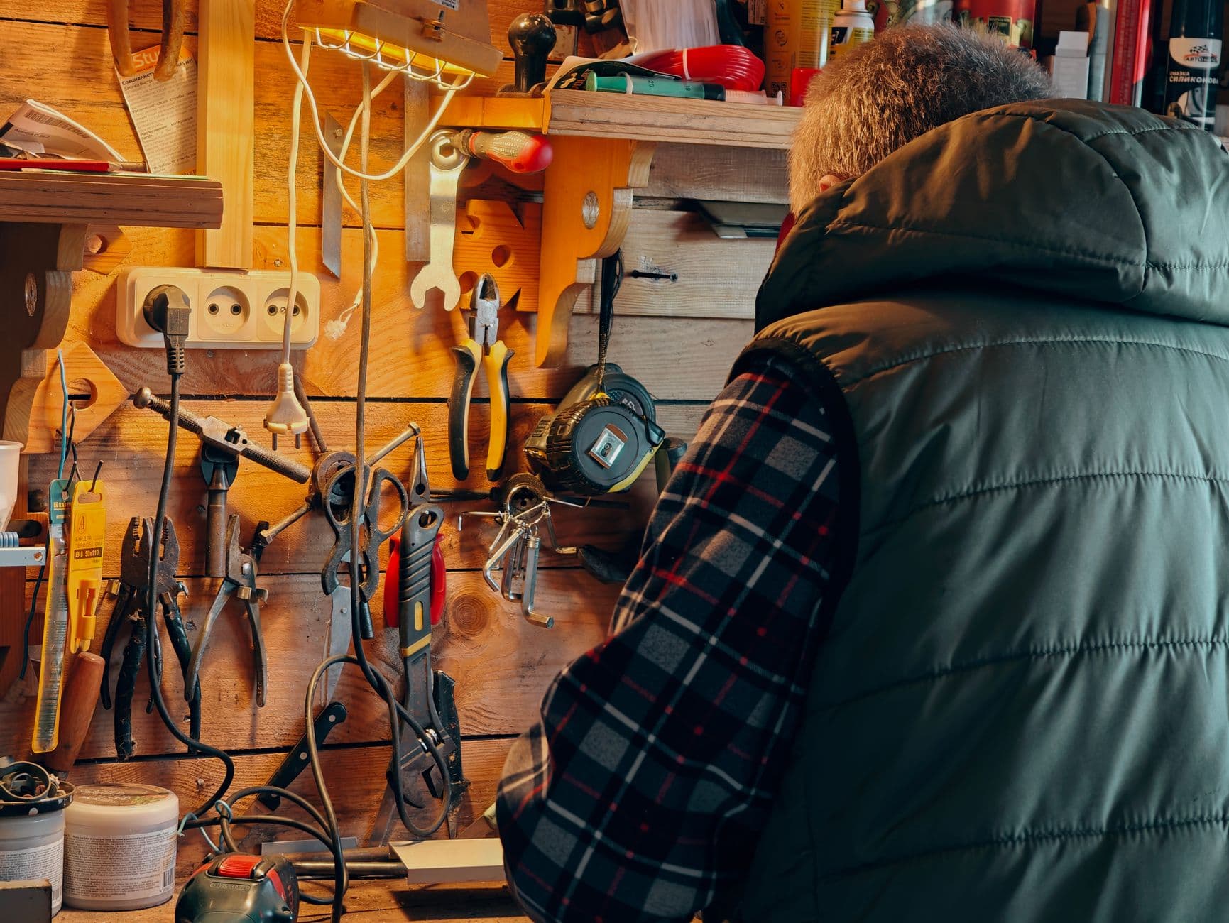 A person working in a wood-paneled workshop surrounded by hanging tools
