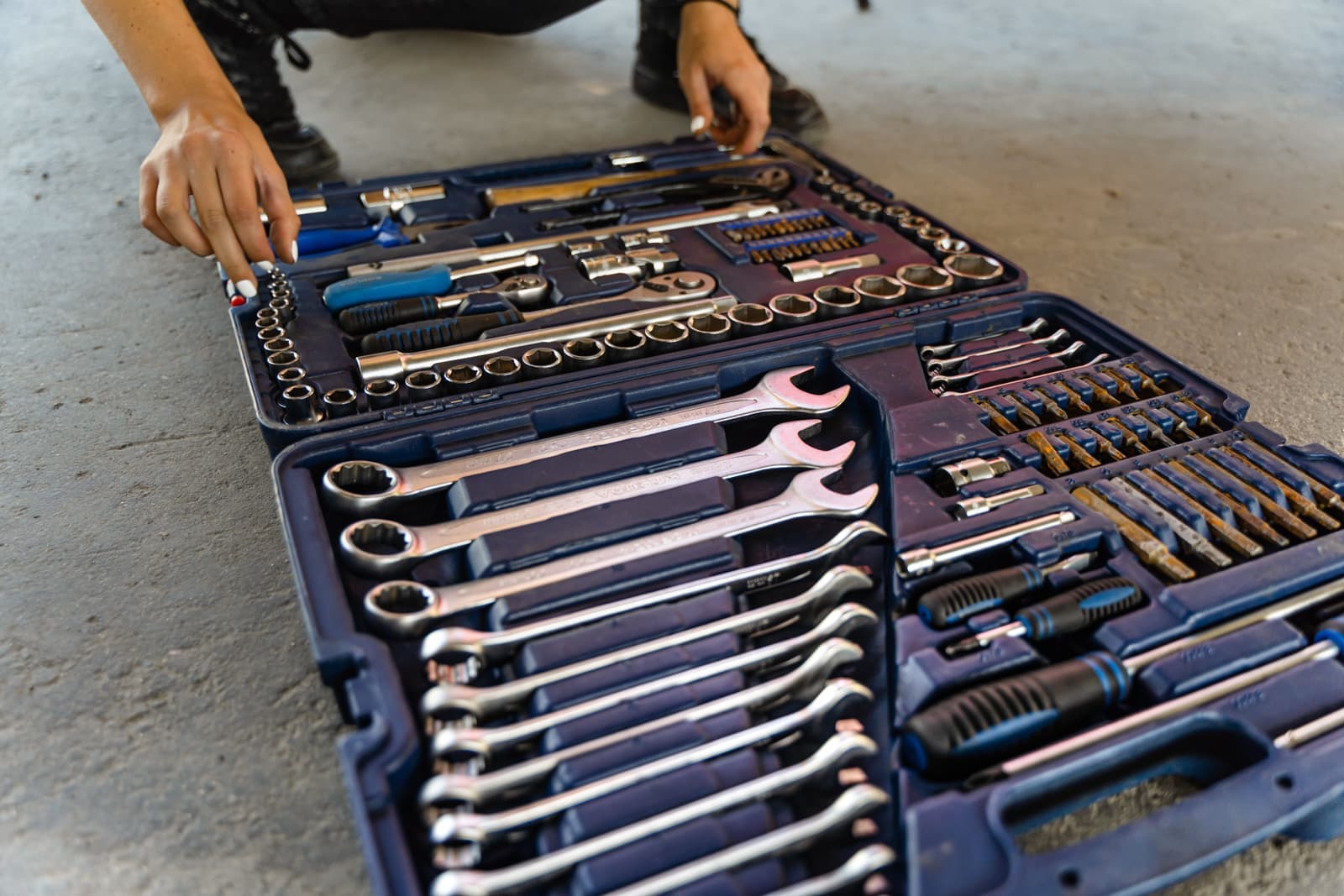 An open toolbox on a concrete floor showing sockets and hand tools