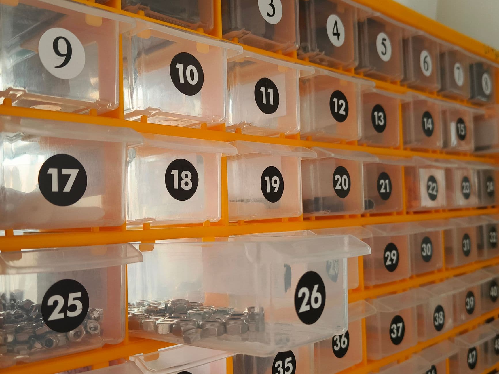 Rows of numbered clear parts bins in an orange wall rack, each holding a different size of nut and washer