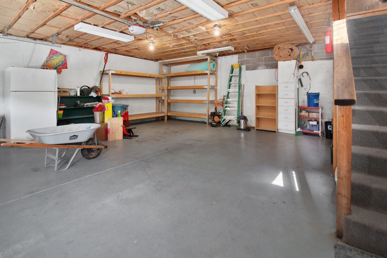 A garage interior with storage shelving, tools and a wheelbarrow along the wall