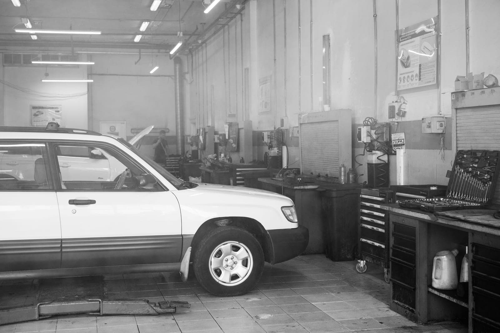 A car in a garage surrounded by tools and equipment, in black and white