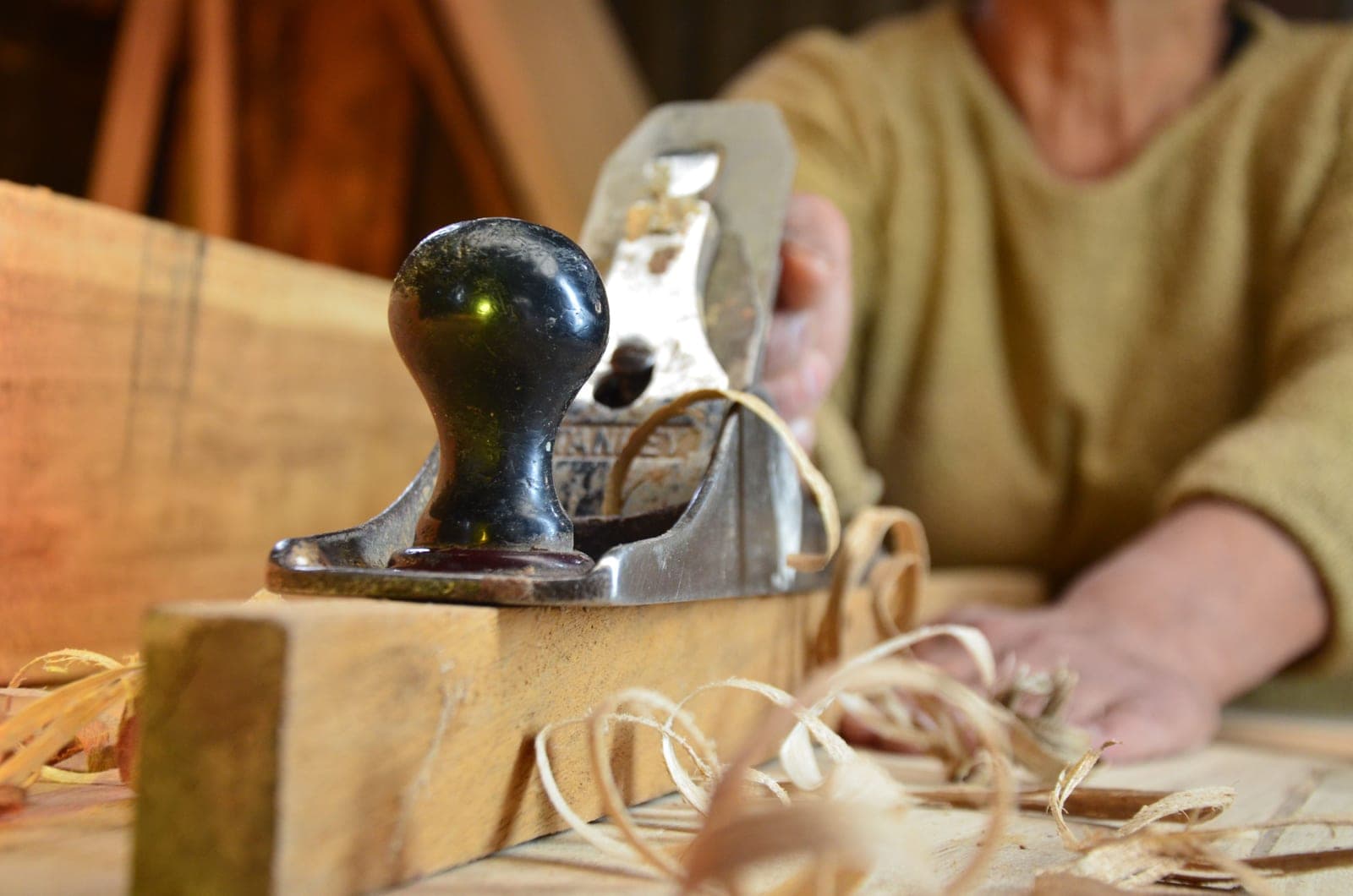 A woodworker shaping a board with a hand plane at the bench