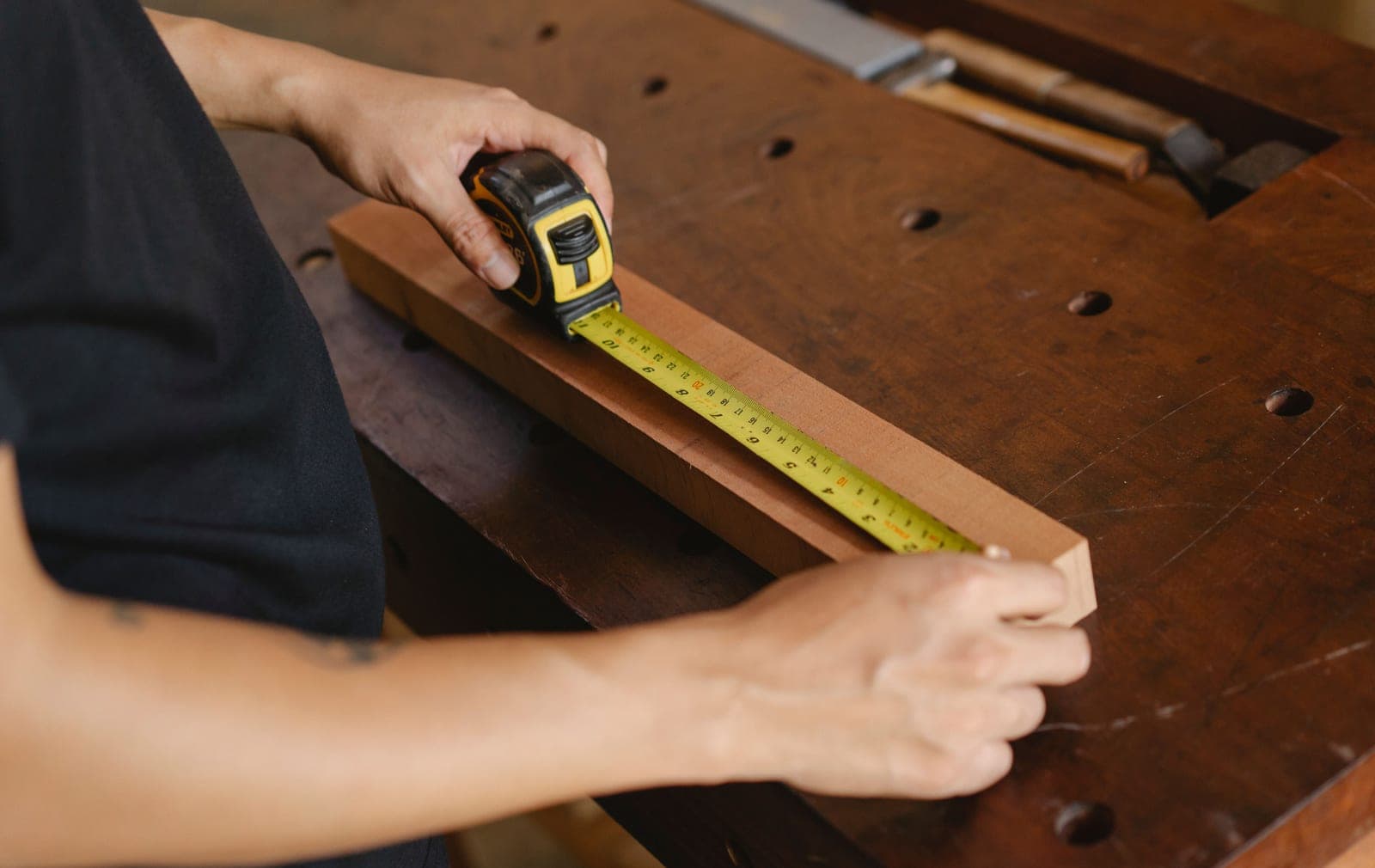 A carpenter measuring a wooden component at a bench
