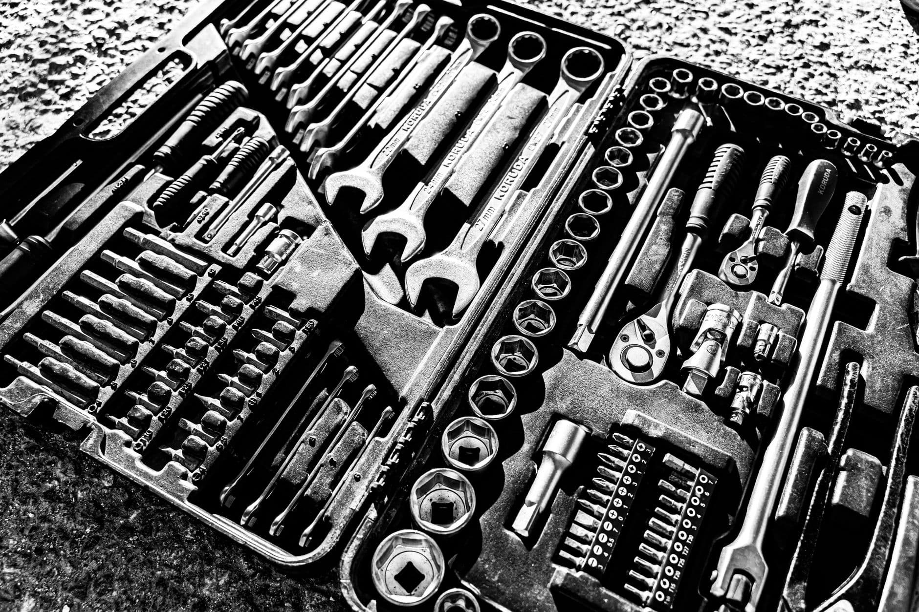 Black and white close-up of combination wrenches, sockets and driver bits held in the molded slots of an open tool case