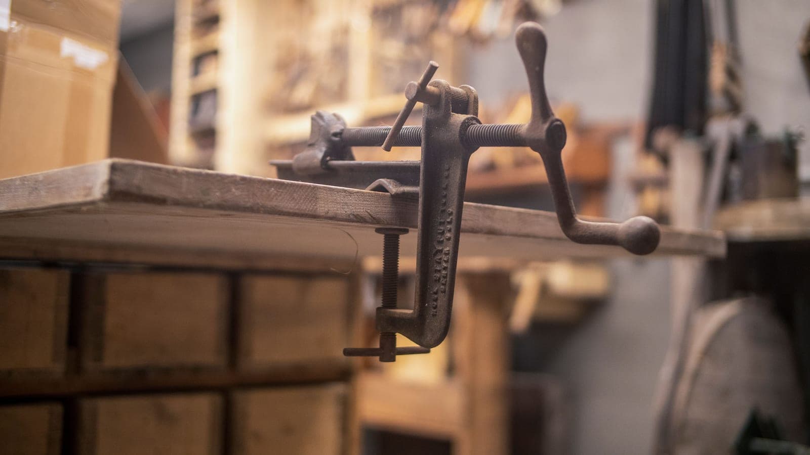 A vintage clamp fixed to the edge of a wooden workbench